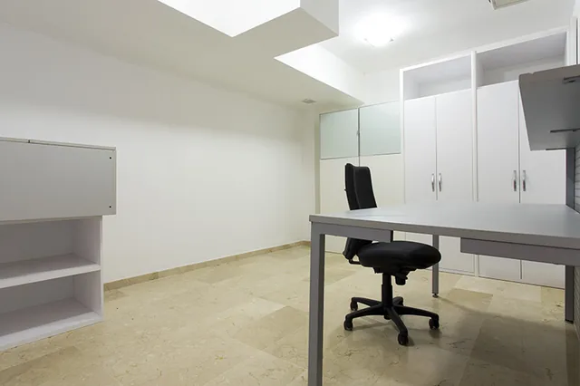 Despacho equipado con mesa, silla, estanterías y armarios blancos